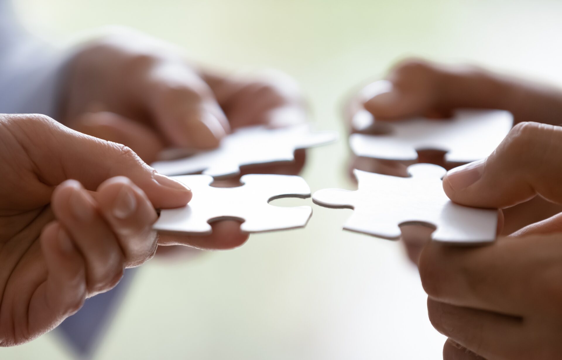 Hands of four businesspeople holding pieces of white puzzles close up