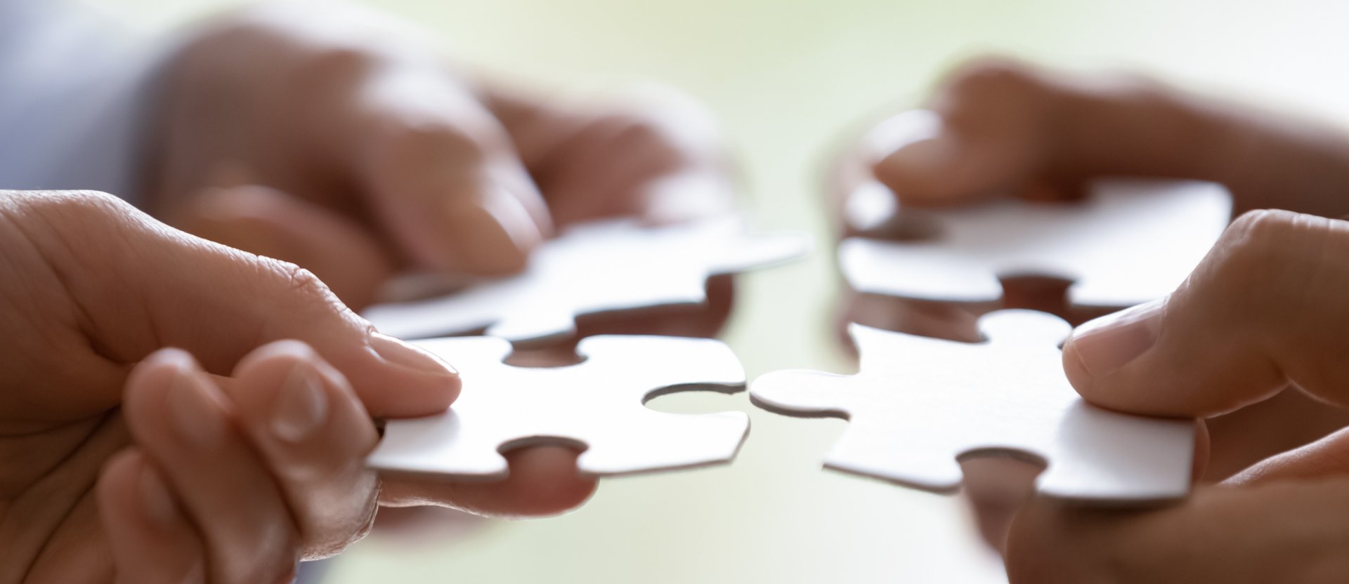 Hands of four businesspeople holding pieces of white puzzles close up